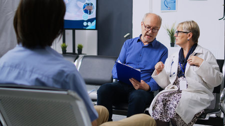 Medic helping patient with medical form in hospital waiting room, discussing health care treatment. Senior man filling insurance documents during checkup visit consultation. Medicine serviceの写真素材