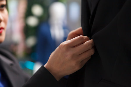 Shopping mall boutique woman employee hands fastening jacket buttons while adjusting apparel merchandise closeup. Clothing store showroom seller arms showcasing garment for saleの写真素材