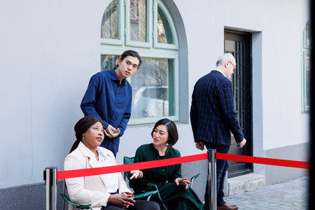 Crowd of diverse people sitting outdoors at shopping center door waiting in line to shop for seasonal holiday sales. Anxious customers at entrance of retail store wait for Black Friday shopping dealsの写真素材