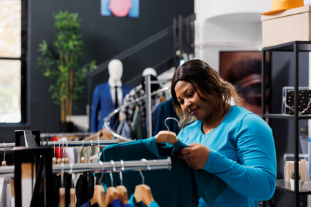 African american woman checking shirt fabric in modern boutique, shopping for fashionable...