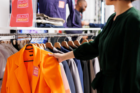 Customer examining clothes hanging on rack in clothing store, doing purchases at shopping mall...