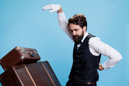Cheerful porter having fun in studio and showing confidence with crazy funny dance moves against blue background. Hotel concierge employee dancing around and being silly in studio.の写真素材