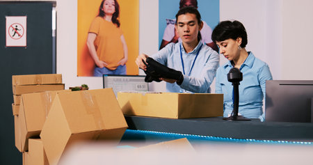 Diverse workers discussing shipping details in modern boutique, preparing packages for delivery. Employees working at customers orders, putting fashionable clothes in carton boxes in shopping centreの写真素材