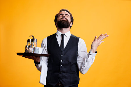 Spiritual waiter talking to jesus in studio, praying for success and fortune while he works in restaurant industry. Professional butler feeling optimistic and positive on camera, pray to god.の写真素材