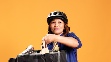 Close up shot of takeaway delivery worker preparing food order while waiting for client to answer door. Courier isolated over studio background taking meal bag out of professional thermic backpackの写真素材