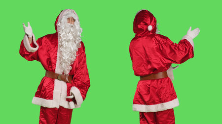 Santa claus cosplay shows advertisement, pointing aside while he poses against greenscreen backdrop with saint nick seasonal costume. Person dressed like father christmas, winter holiday marketing.の写真素材