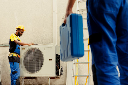 Engineer arriving on location to help apprentice mend busted electric coils in damaged external air conditioner. Technicians comissioned to prevent internal parts breakdowns, ensuring timely repairの写真素材