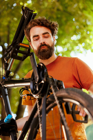 Close-up of caucasian male cyclist securing his bike wheel ensuring a safe and enjoyable recreational cycling experience. Outdoor activity of young athletic man maintaining bicycle tire and chain ring.の写真素材