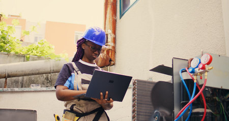 Certified technician working on outdoor hvac system, holding laptop. Competent mechanic optimizing...