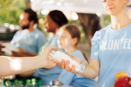 Young volunteers compassionately distribute food boxes, providing assistance to the poor. Detailed image of female charity worker giving water and fresh fruits to the needy, less fortunate individual.の写真素材