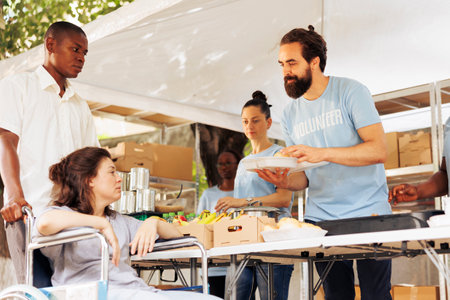 Volunteers happily provide food to diverse needy individuals, homeless, sick, disabled. Image...
