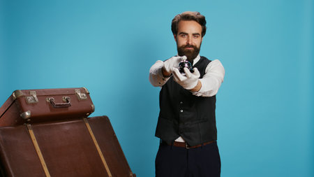 Stylish bellboy with luggage and bell, using to ring for concierge service at hotel in tourism sector. Doorkeeper porter handling trolley bags to help guests, classy elegant occupation.の写真素材