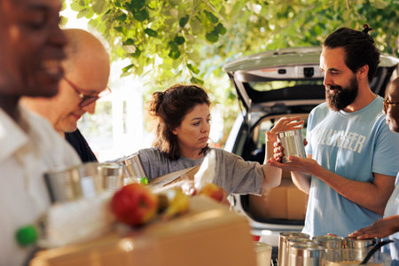 Group of volunteers including African American and Caucasian individuals distribute donated food to homeless and needy. Charity workers support hunger relief and provide essential aid to community.の写真素材