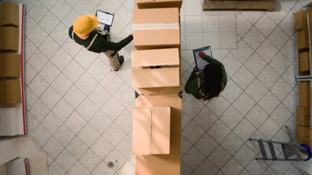 Top down view of warehouse logistics coordinators examining cardboard box parcels in parallel,...