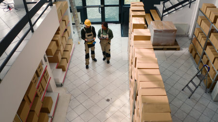 Aerial drone shot of warehouse employees starting shift, inspecting cardboard box parcels before clearing them for shipping. Repository executives making sure stocks and inventory are well organizedの写真素材