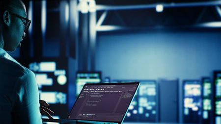 Manager overseeing data center, running code on laptop, troubleshooting and upgrading technologically advanced infrastructure designed to accommodate servers, networking systems and storage arraysの写真素材