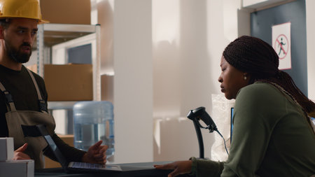Repository warehouse director carrying out the logistics of receiving, processing, storing and sending inventory according to purchase orders and shipping schedules, helped by african american womanの写真素材