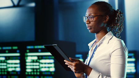 African american woman walking through server farm rows providing processing resources for different workloads. Admin fixing data center rackmounts tasked with solving complex operationsの写真素材