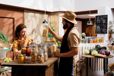 Client shopping for pantry staples in environmentally conscious zero waste store, being assisted with advice by trader. Merchant showing woman ecological nonpolluting productsの写真素材