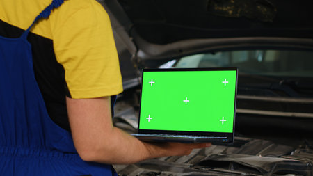 Certified mechanic using mockup laptop in car service to order new parts for damaged vehicle. Close up shot of specialist using device with isolated screen to look online for replacing componentsの写真素材