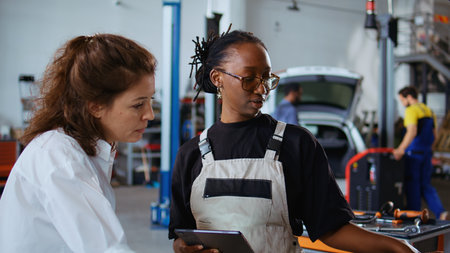 Repair shop workers brainstorming ways to fix car, using tablet and laptop. Colleagues servicing...