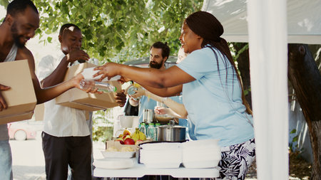 In a sunny day, multiethnic volunteers distribute donations of food to the needy, offering help and hope to homeless people. Caring charity workers giving hunger relief packages to the less fortunate.の写真素材
