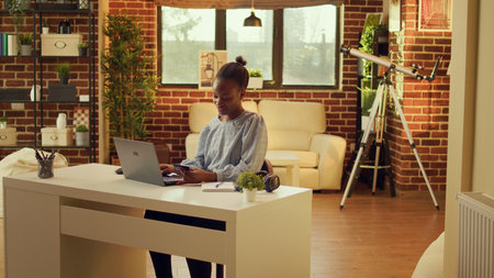 Excited woman does online shopping at home, carefully typing credit card information on laptop. African american person adding payment method on webpage, sitting in warm space at sunset.の写真素材
