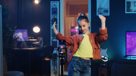 Kid doing viral dance choreography in living room with 3D rendered animations on computer screens in background. Child dancing in neon lit home studio interior, producing content with cellphoneの写真素材