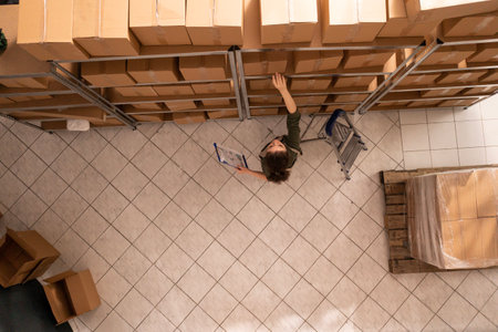 Stockroom worker preparing packages using cardboard boxes, working at clients orders in storage room. Warehouse employee checking products during storehouse inventory, analyzing goods checklistの写真素材