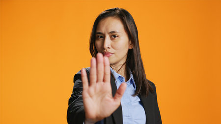 Filipino woman showing stop sign with palm, advertising negativity and no symbol on camera. Female model wearing formal attire in studio, showcasing rejection and refusing something.の写真素材