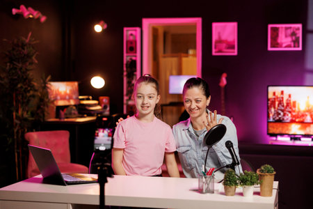 Daughter and mother using phone on tripod to film family vlog in home studio, talking about school....