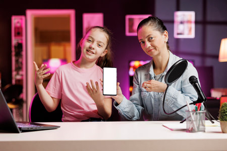 Media star daughter and mother excited to review newly launched mockup smartphone, comparing features with older models. Young internet show host filming video analyzing isolated screen smartphoneの写真素材