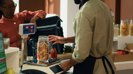 Seller preparing food order for delivery, putting fresh organic groceries in thermal backpack. African american woman coming to pick up merchandise for local eco store customers.の写真素材