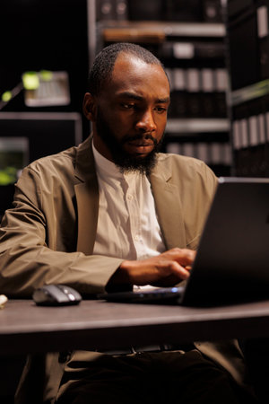 Concentrated private detective checking evidence using laptop while working overtime in dark agency office. Investigator reading police records on computer, searching insight for solving crimeの写真素材
