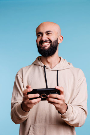 Excited arab man laughing while playing online game using smartphone app. Smiling gamer enjoying...