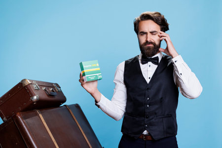 Sick worker displaying package of drugs against blue background while struggling with headache and using medication for pain relief. Concierge at hotel takes analgesics as he feels ill.の写真素材