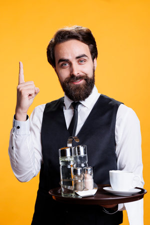 Professional employee having new idea in studio, posing with index finger up and indicating upwards direction with restaurant tray in hand. Skilled butler or waiter feeling genious, innovative.の写真素材