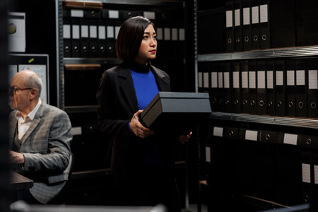 Professional asian accountant storing administrative analytical data paperwork boxes in cabinet room office. Professional businesswoman in file storage bureaucratic workplaceの写真素材