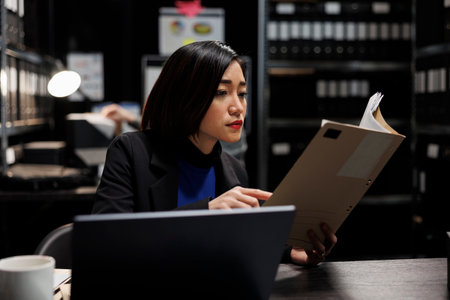 Asian businesswoman executive checking accountancy budget plan data paperwork. Bureaucratic administration employee in repository filled with document folders and graphical chart reportsの写真素材