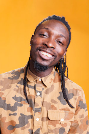 Attractive joyful man smiling at camera, having fun while posing over yellow background. Relaxed african american person with positive facial expression, enjoying free time during studio shotの写真素材