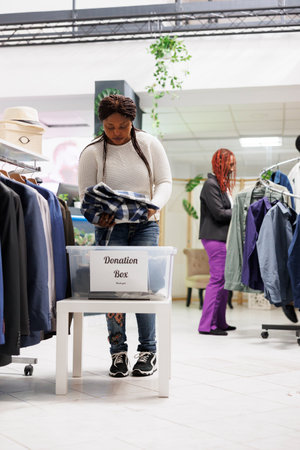 African american customer donating clothes to welfare organization in shopping center. Woman putting...