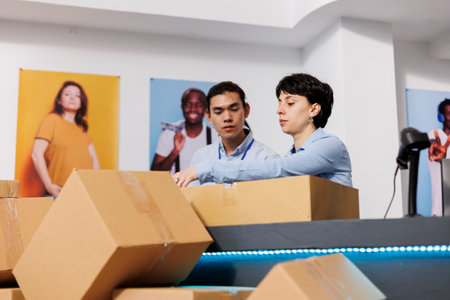 Diverse employees working at customers orders, preparing packages for delivery in modern boutique. Workers putting fashionable clothes in carton boxes, discussing shipping detalis at counter deskの写真素材