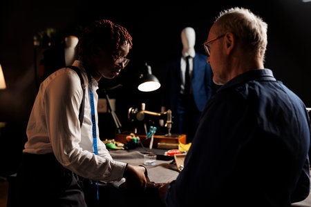 Attentive african american apprentice carefully listening to master dressmaker guiding her with cutting fabric. Couturiers manufacturing upcoming bespoken fashion collectionの写真素材