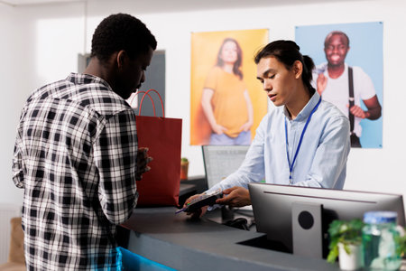 African american man paying for stylish clothes with credit card at counter desk in modern boutique. Shopaholic customer shopping for casual wear, buying fashionable merchandise in clothing storeの写真素材