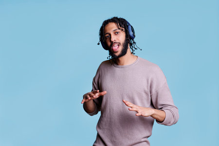 Carefree arab dancer moving body while listening to music in wireless headphones portrait. Young cheerful person enjoying song in earphones, dancing and looking at cameraの写真素材