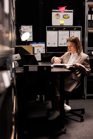 Police officer analyzing crime scene files, working overtime at criminal case in arhive room....