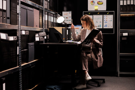 Inspector reading police report, working late at night at criminal case in arhive room. Private detective analyzing crime scene evidence, trying to catch mysterious suspect. Law enforcement conceptの写真素材