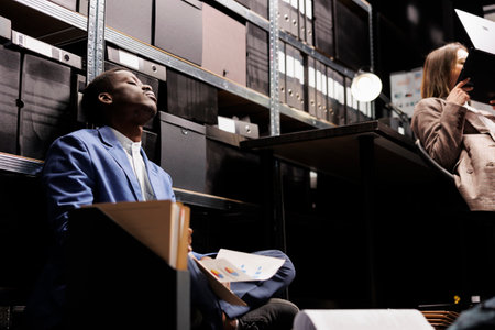 Officers working at agency investigation, analyzing victim report in arhive room. Tired inspectors searching clue using crime scene files trying to crack case and bring the suspect to justice.の写真素材