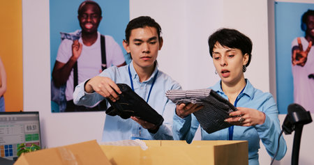 Diverse store managers preparing packages for shipping, putting stylish clothes in carton boxes in modern boutique. Employees working at clients orders, discussing delivery details in shopping mallの写真素材