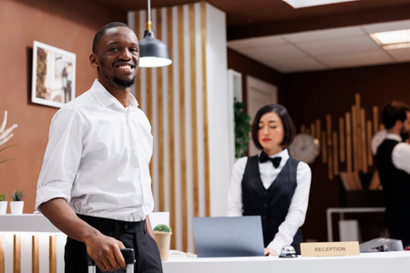 Male tourist sitting at front desk to register and fill in check in forms, guest smiling and waiting for hotel service. Young man standing near reception counter in lobby, luxury resort.の写真素材